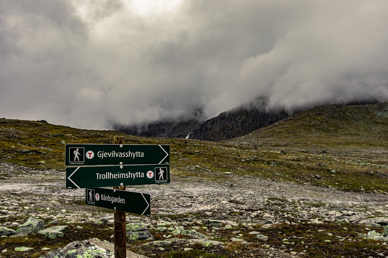 Mountain trail signage in Gjevilvasshytta, TrÃ¸ndelag, Norway amidst cloudy skies.